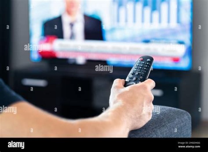 Man watching tv news program and sitting on couch home. Television remote control in hand. Politics, business or finance network channel. Online live broadcast in monitor screen. Morning newscast.